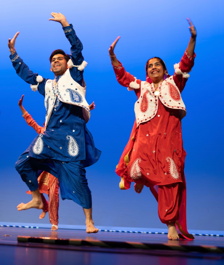 Avneet and a teammate mid-performance on stage in red and blue bhangra outfits
